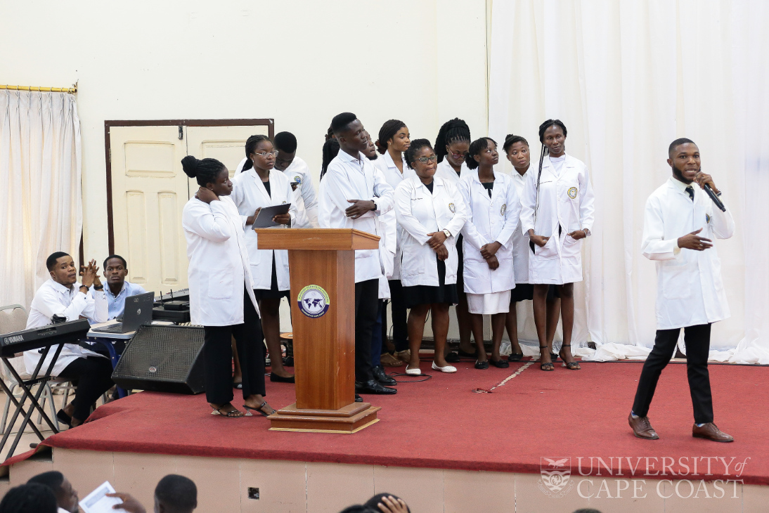 Students standing on a podium, wearing white jackets